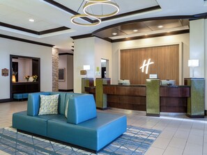 A lobby with a reception desk, a blue sofa, and a decorative wall with a logo. - Holiday Inn Chicago Northwest-Elgin by IHG (Elgin)