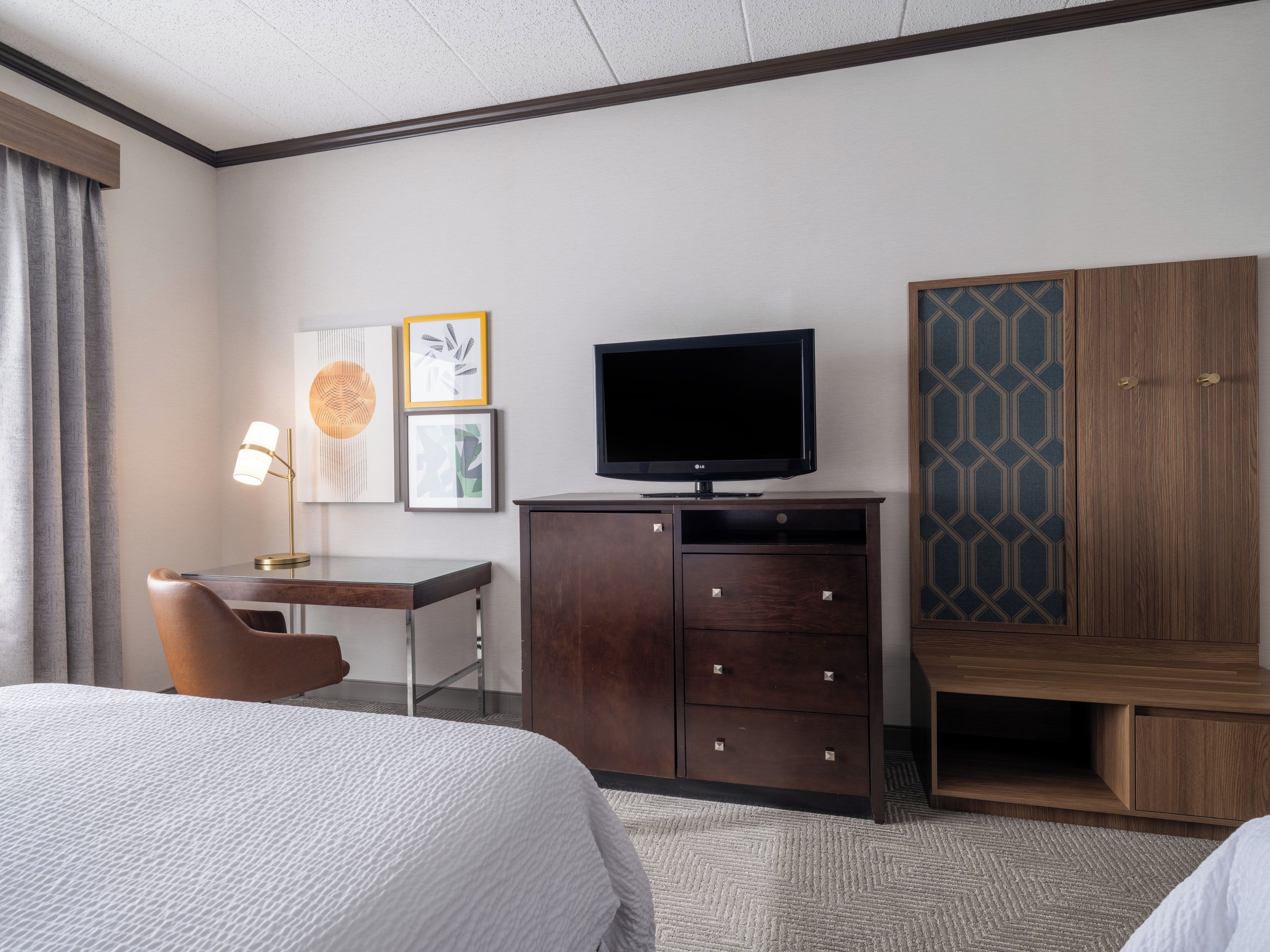 Une chambre d’hôtel comprenant un lit, un bureau avec une lampe, une télévision et une armoire.