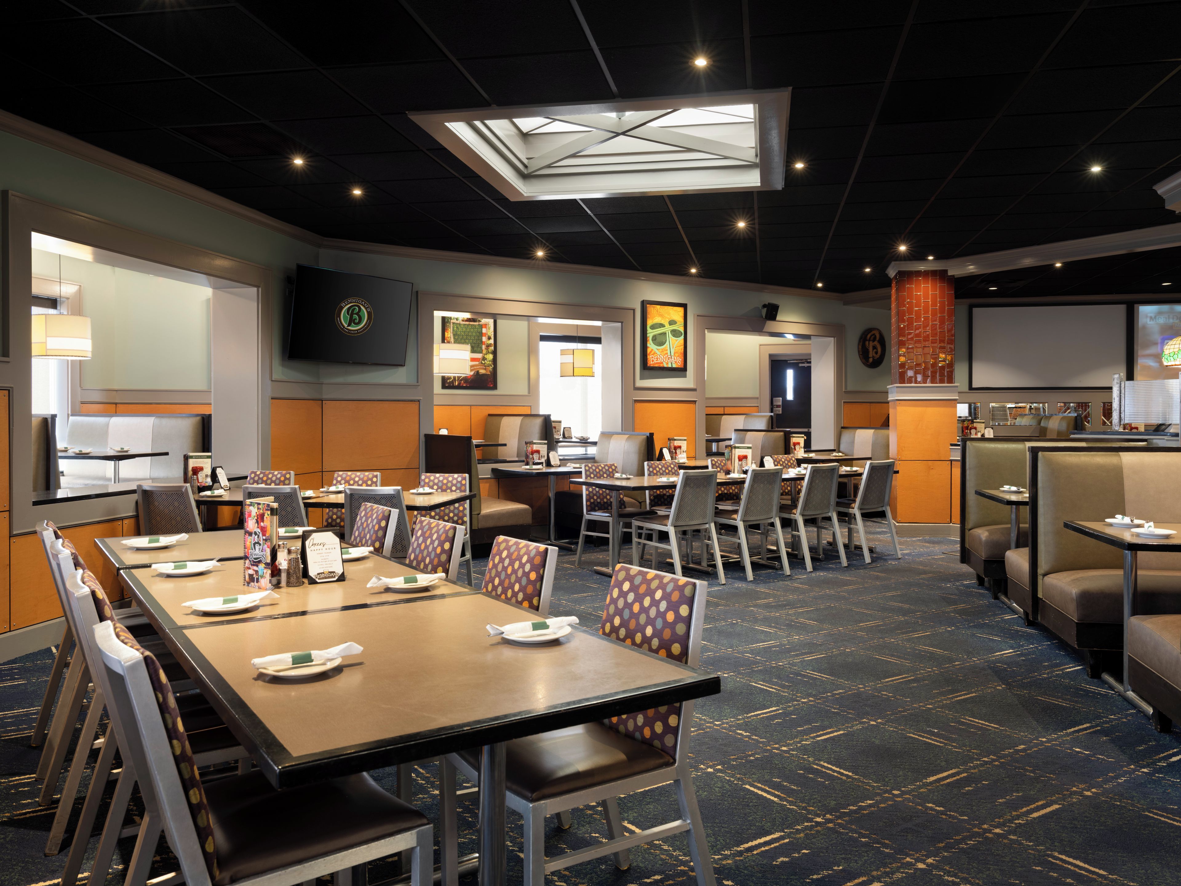 A hotel dining area with multiple tables and chairs, a large screen, and a skylight.