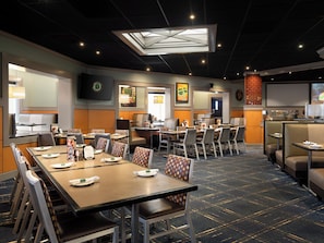A hotel dining area with multiple tables and chairs, a large screen, and a skylight.