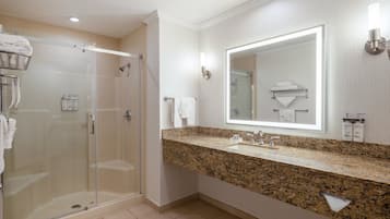 Un baño moderno con ducha de vidrio, encimera de granito y un espejo grande.