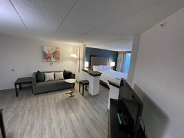 Una habitación de hotel con cama, sofá, mesita, televisor y un cuadro en la pared.