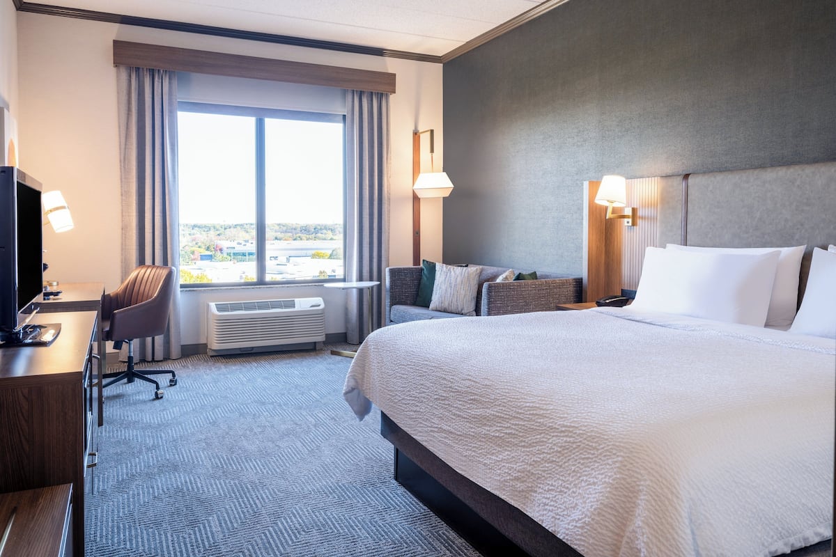 A hotel room with a large bed, a desk with a computer, a chair, and a window with curtains.