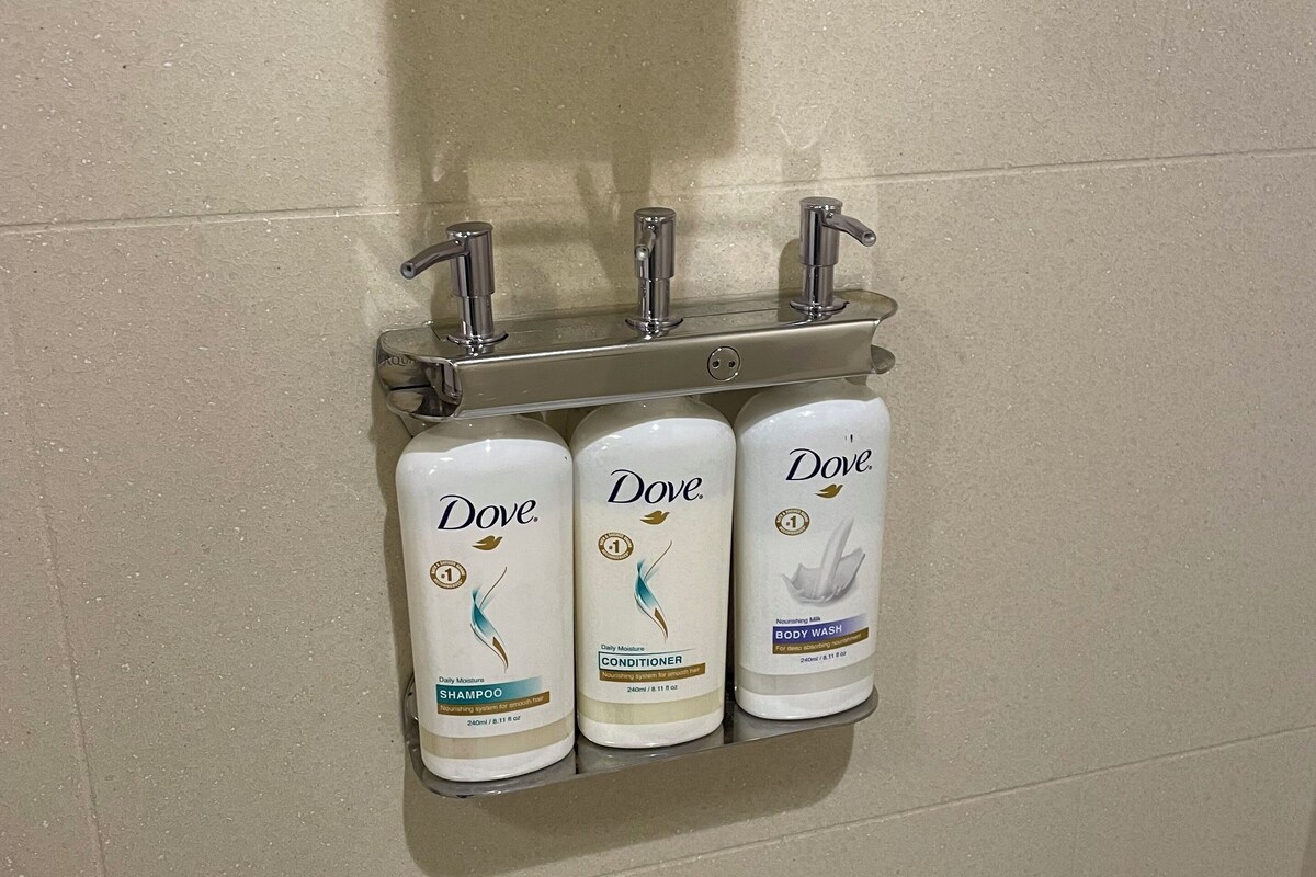A bathroom with a wall-mounted shelf holding three Dove personal care products: shampoo, conditioner, and body wash.