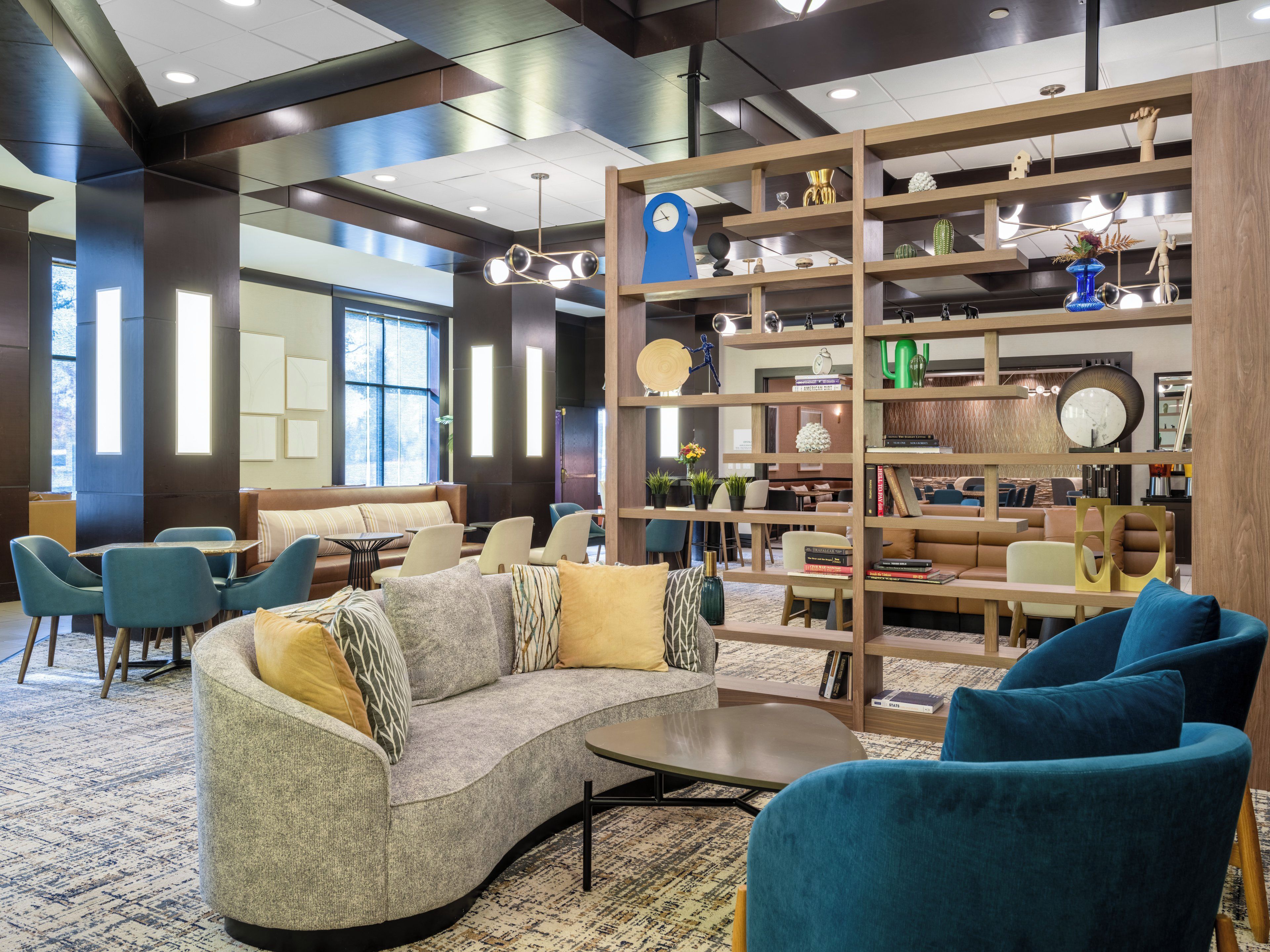 A modern interior with a curved sofa, blue armchairs, and a wooden bookshelf filled with decorative items.