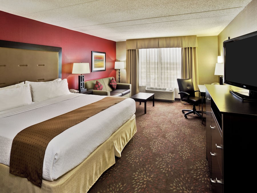 A hotel room with a large bed, a desk, a chair, a television, and a window with curtains.
