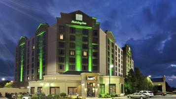 A Holiday Inn hotel with a prominent sign, multiple floors, and a parking lot with cars.