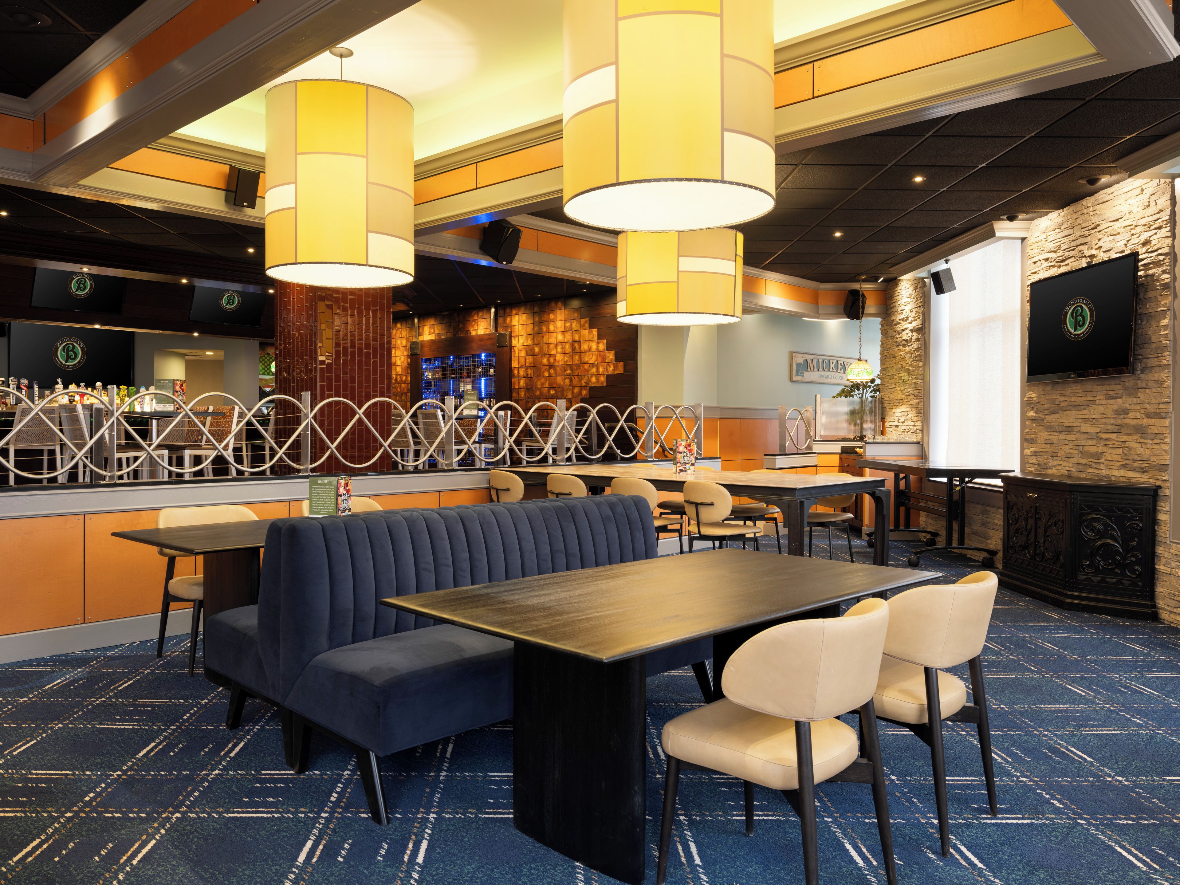 Un restaurante con cabinas, mesas y sillas. Hay una zona de bar con mostrador y taburetes.