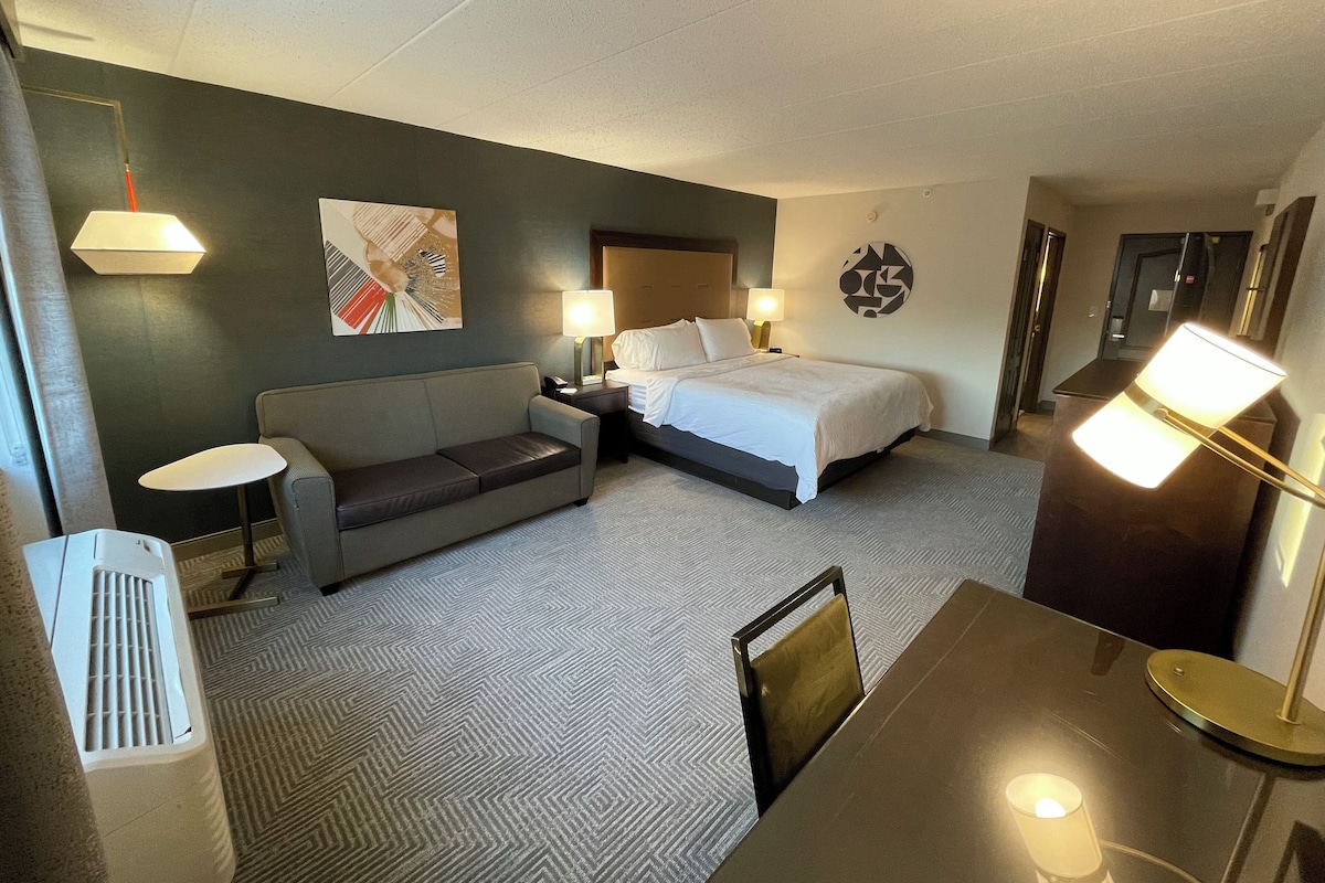A hotel room with a bed, a sofa, a small table, and a chair.