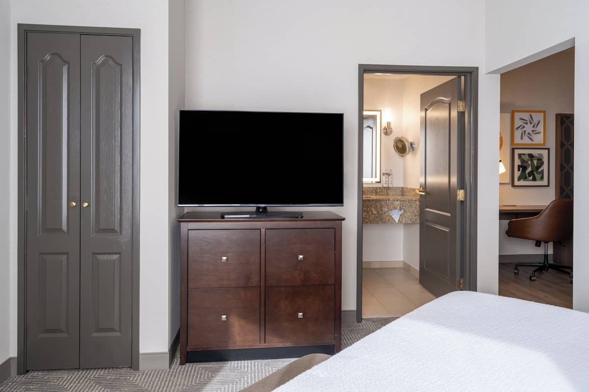 A hotel room with a bed, a TV, a dresser, and a desk with a chair.