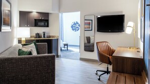 Une chambre d’hôtel moderne dotée d’un espace salon, d’une kitchenette et d’un grand téléviseur.