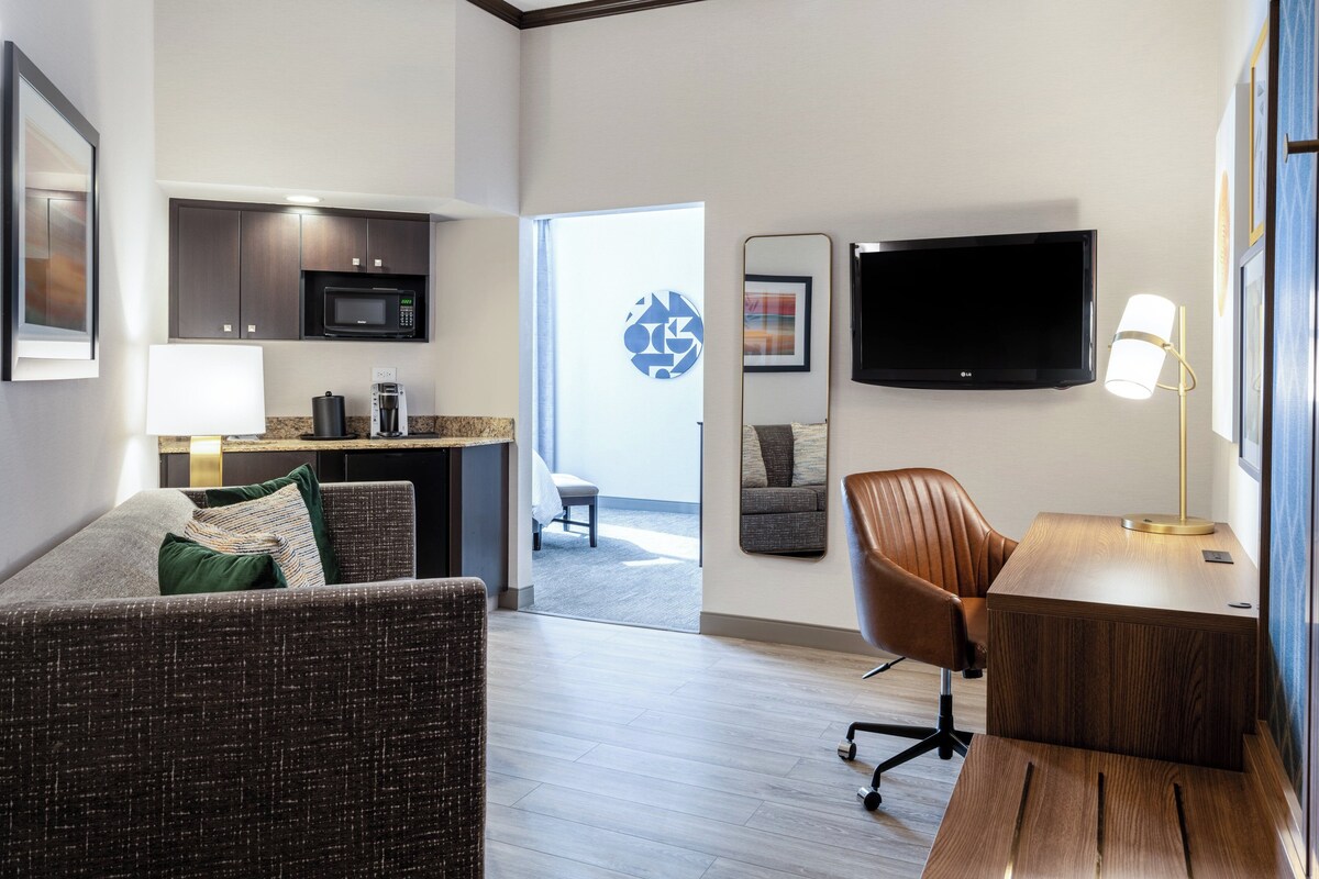 A modern hotel room with a living area, kitchenette, and a large TV.