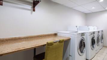 A laundry room with a wooden bench, a chair, and multiple washing machines.