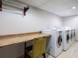 Una sala de lavandería con un banco de madera, una silla y varias lavadoras.