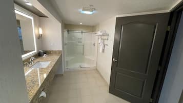 A bathroom with a glass-enclosed shower, a sink with a mirror, and a door.