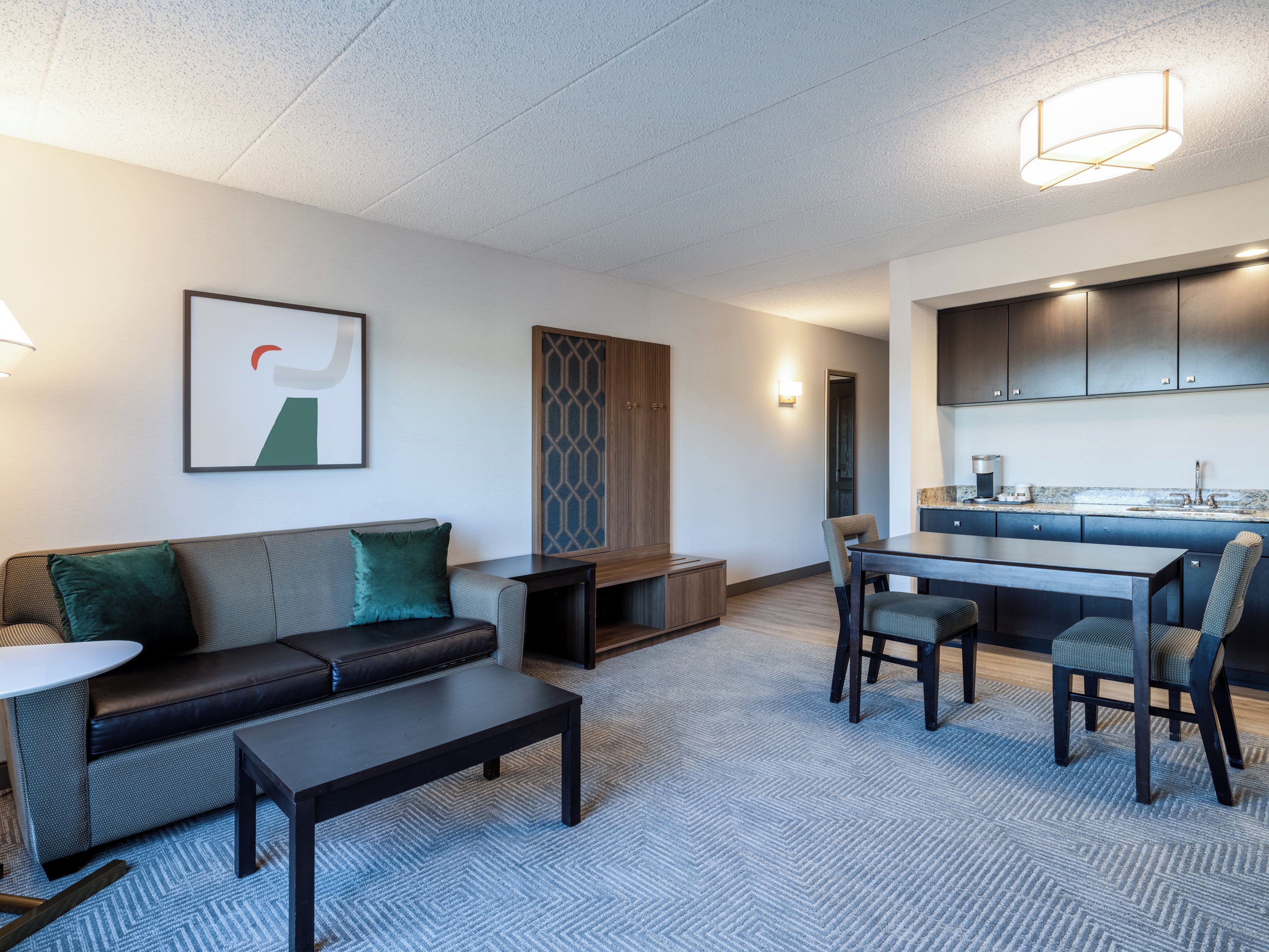 A modern hotel room with a living area, a dining table, and a kitchenette.