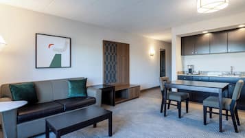 A modern hotel room with a living area, a dining table, and a kitchenette.