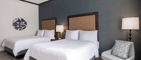 A hotel room with two beds, a chair, a lamp, and a wall art piece.