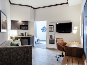 A modern hotel room with a living area, kitchenette, and a large TV.