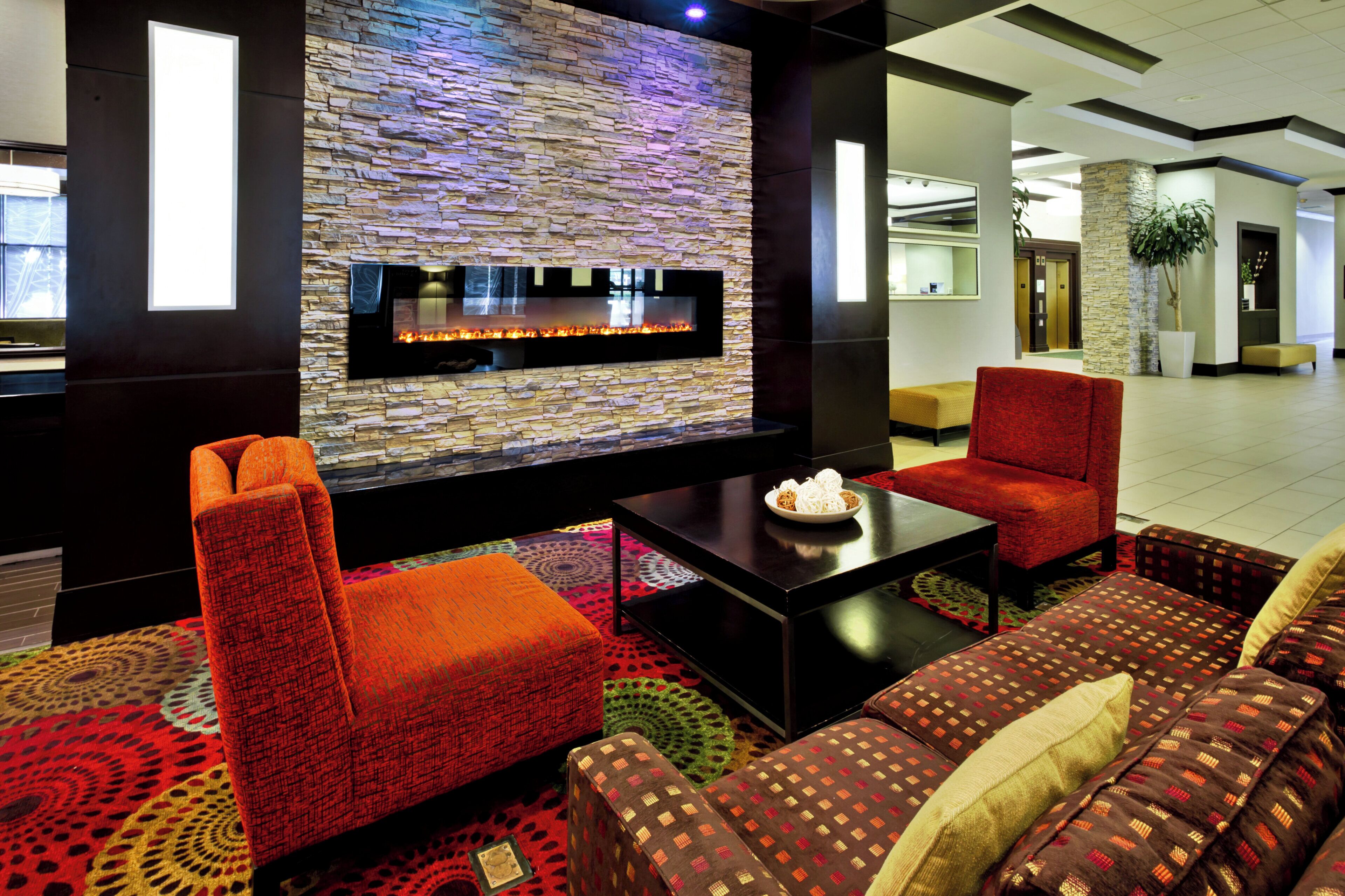 A modern lounge area with a stone wall fireplace, comfortable seating, and a patterned carpet.