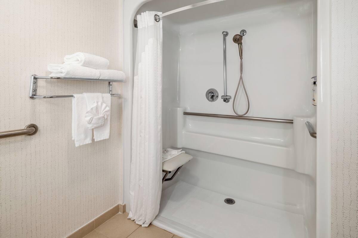 A walk-in shower with a glass door, a towel rack with folded towels, and a shower control panel.