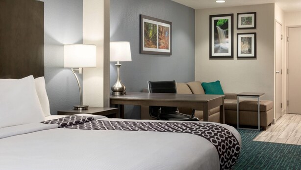 Een hotelkamer met een bed, een bureau, twee stoelen, een lamp en ingelijste foto's aan de muur.