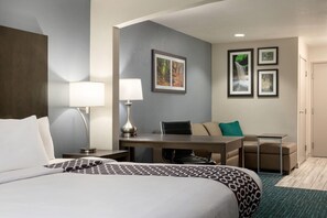 Una habitación de hotel con cama, escritorio, dos sillas, lámpara y cuadros en la pared.