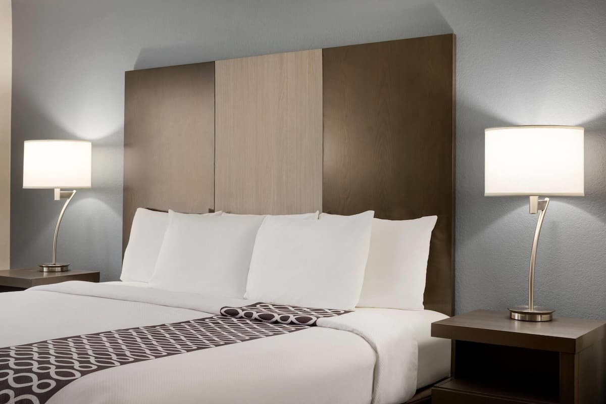 Een hotelkamer met een groot bed, twee nachtkastjes met lampen en een bedsprei met een patroon.