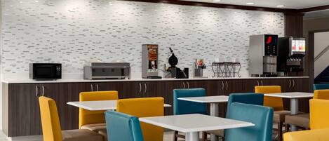 A modern hotel restaurant with a patterned backsplash, microwave, coffee machine, and a water dispenser.