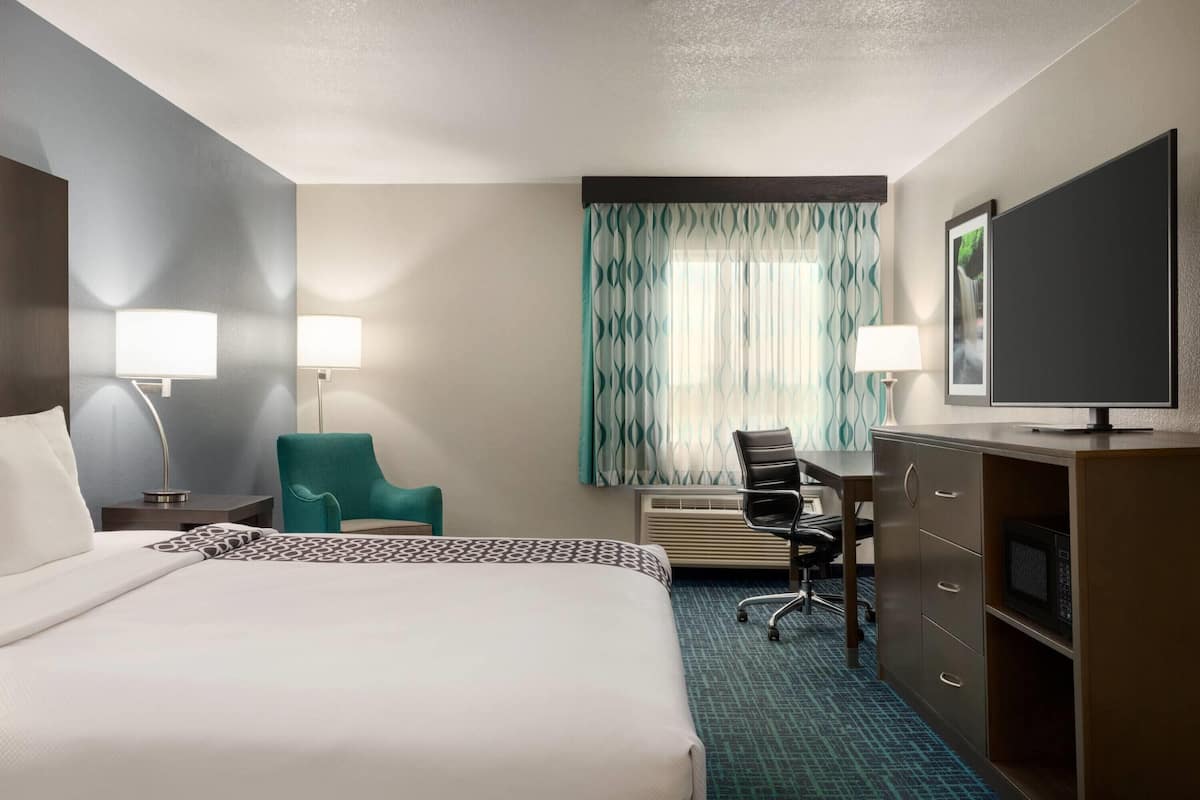 Een hotelkamer met een groot bed, een bureau met stoel, een televisie en een kledingkast.