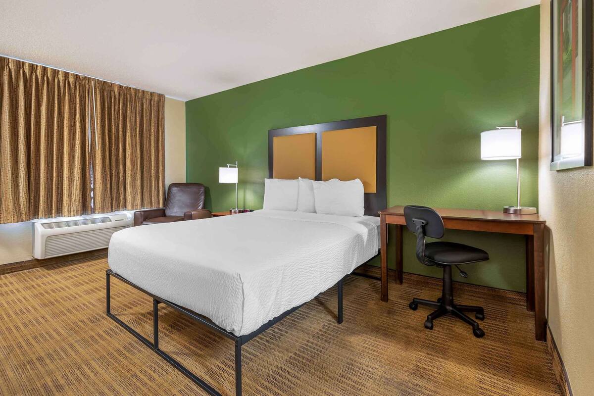 Una camera d'albergo con un letto, una scrivania, una sedia e un'ampia finestra con tende.