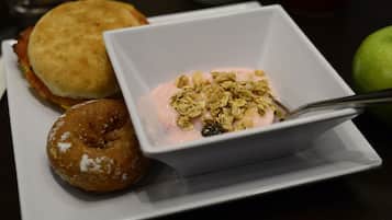 Ein Teller mit einem Sandwich, einem Donut und einer Schale Joghurt mit Granola.