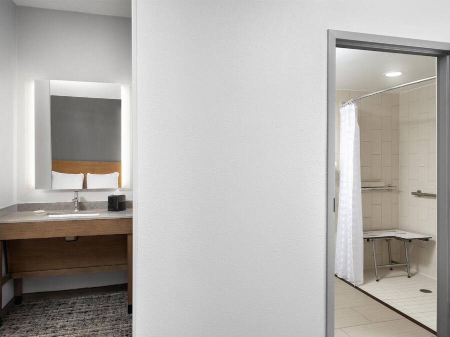 Un baño moderno con tocador de madera, un espejo y una zona de ducha visible a través de una puerta abierta.