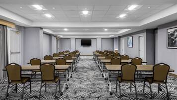 A conference room with a long table, chairs, a flat-screen TV, and patterned carpet.