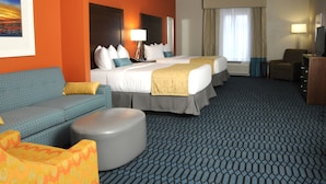 A hotel room with two beds, a sofa, a small ottoman, and a television.