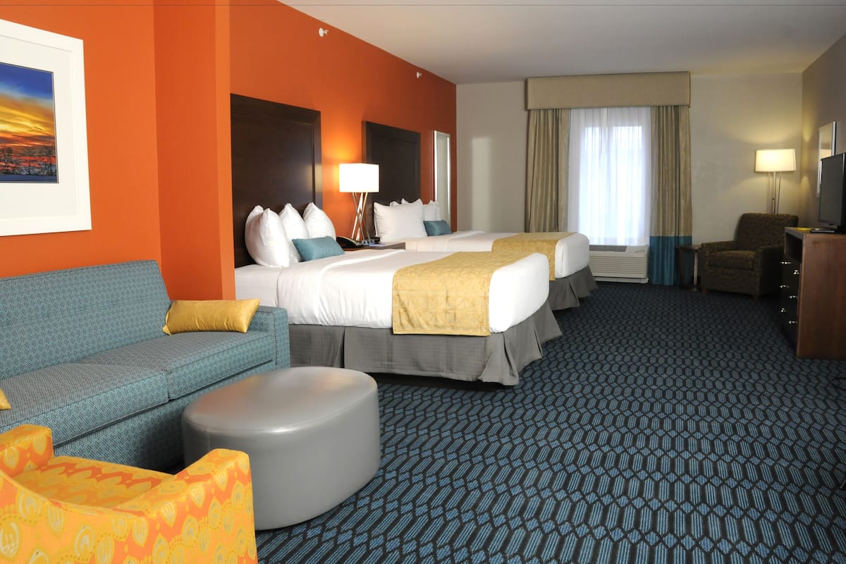 A hotel room with two beds, a sofa, a small ottoman, and a television.