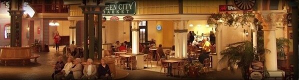 A bustling indoor market with a green sign reading "Queen City Market."