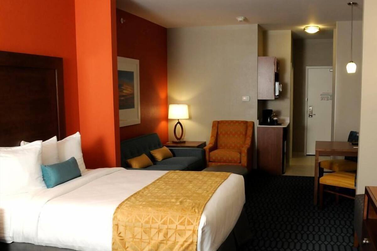 A hotel room with a bed, a sofa, a chair, a desk, and a kitchenette.