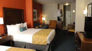 Hotelkamer met een groot bed, een kleiner bed, een bureau met stoel, een televisie en een lamp.