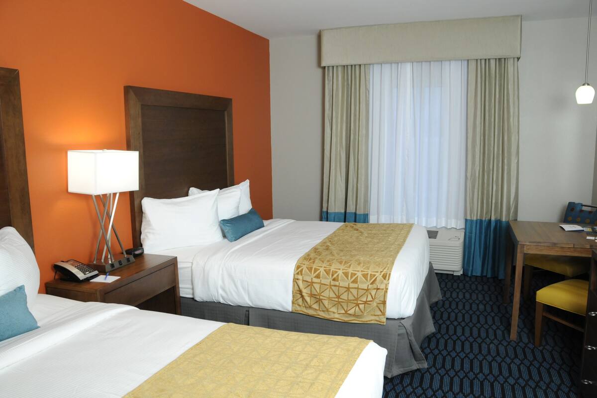 A hotel room with two beds, a desk, a lamp, and a telephone.