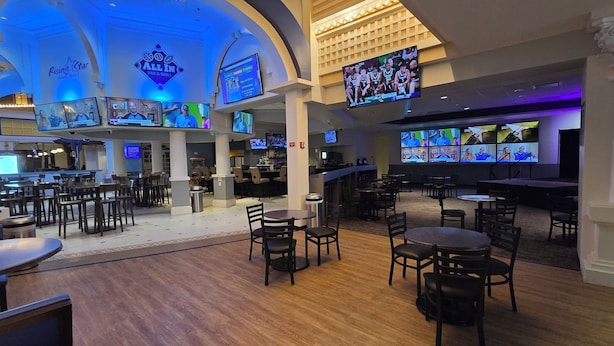 A spacious bar area with multiple screens displaying sports events, a variety of seating arrangements, and a prominent 'Rising Star Casino & Resort' sign.