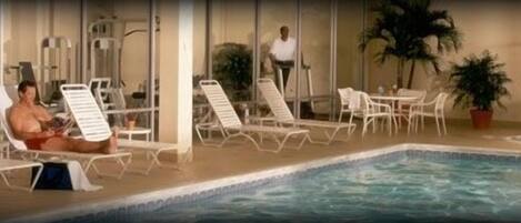 A pool area with lounge chairs and a person in the water.