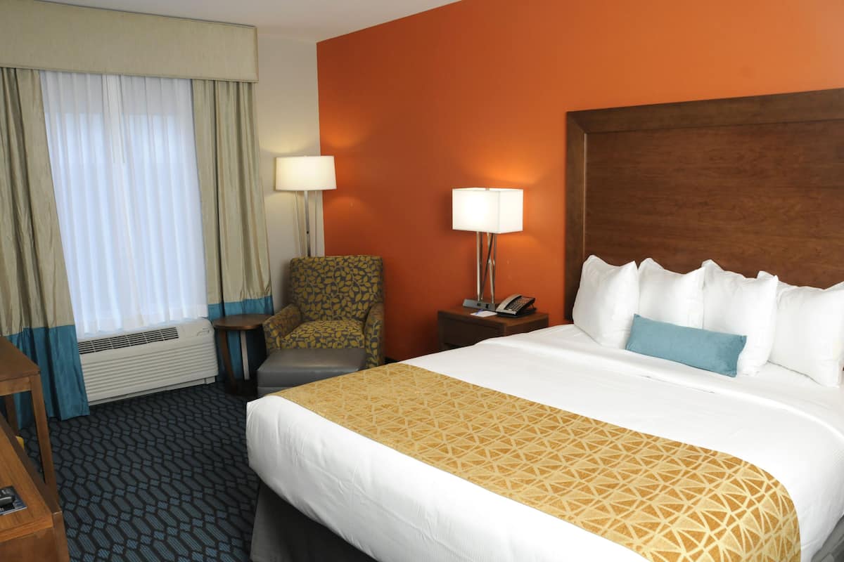 A hotel room with a large bed, a chair, a desk, and a lamp.