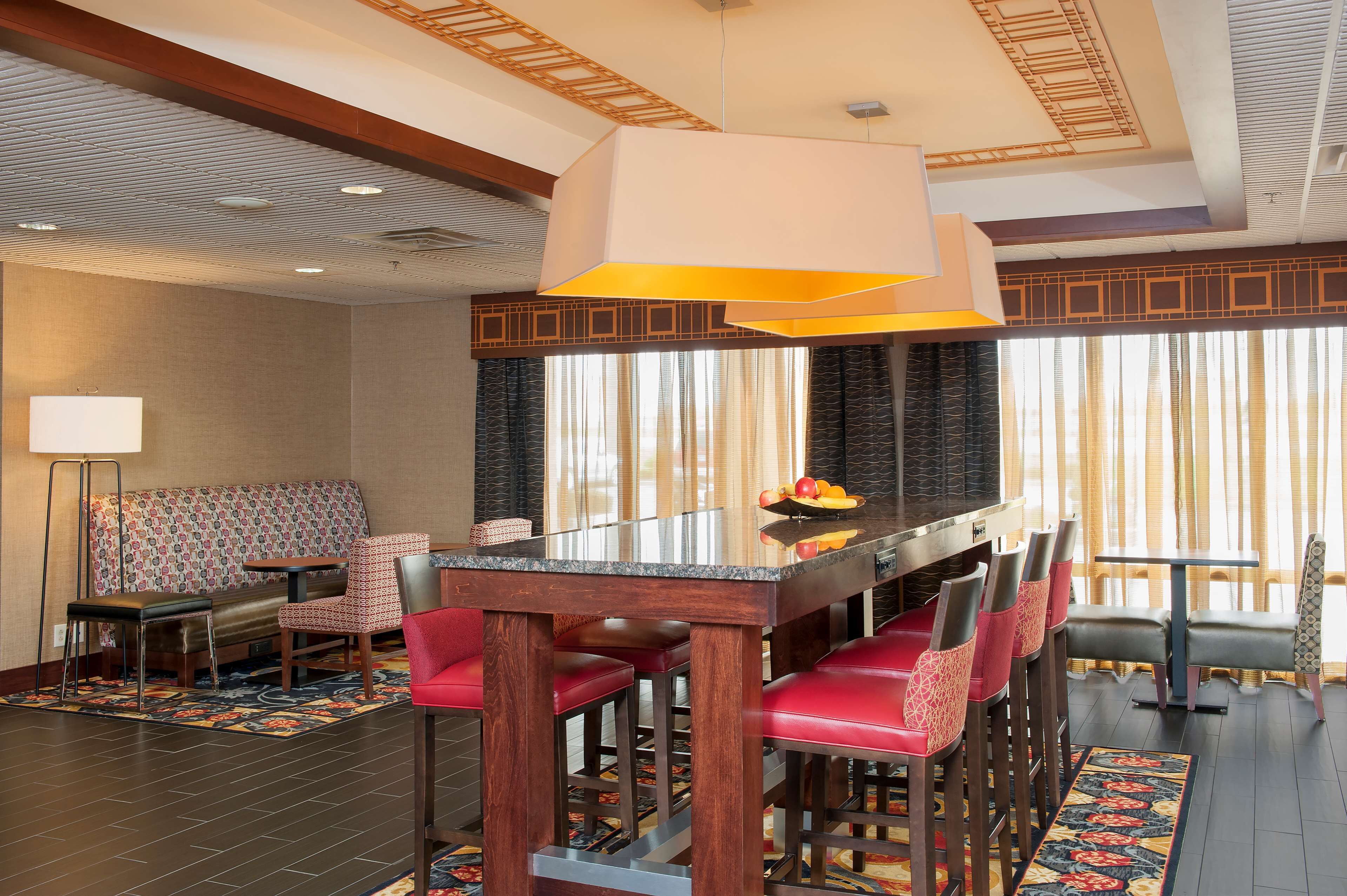 A modern dining area with a glass-top table, red upholstered chairs, and a patterned rug.