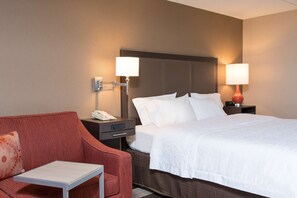 A hotel room with a bed, a red armchair, a small table, and two bedside lamps.