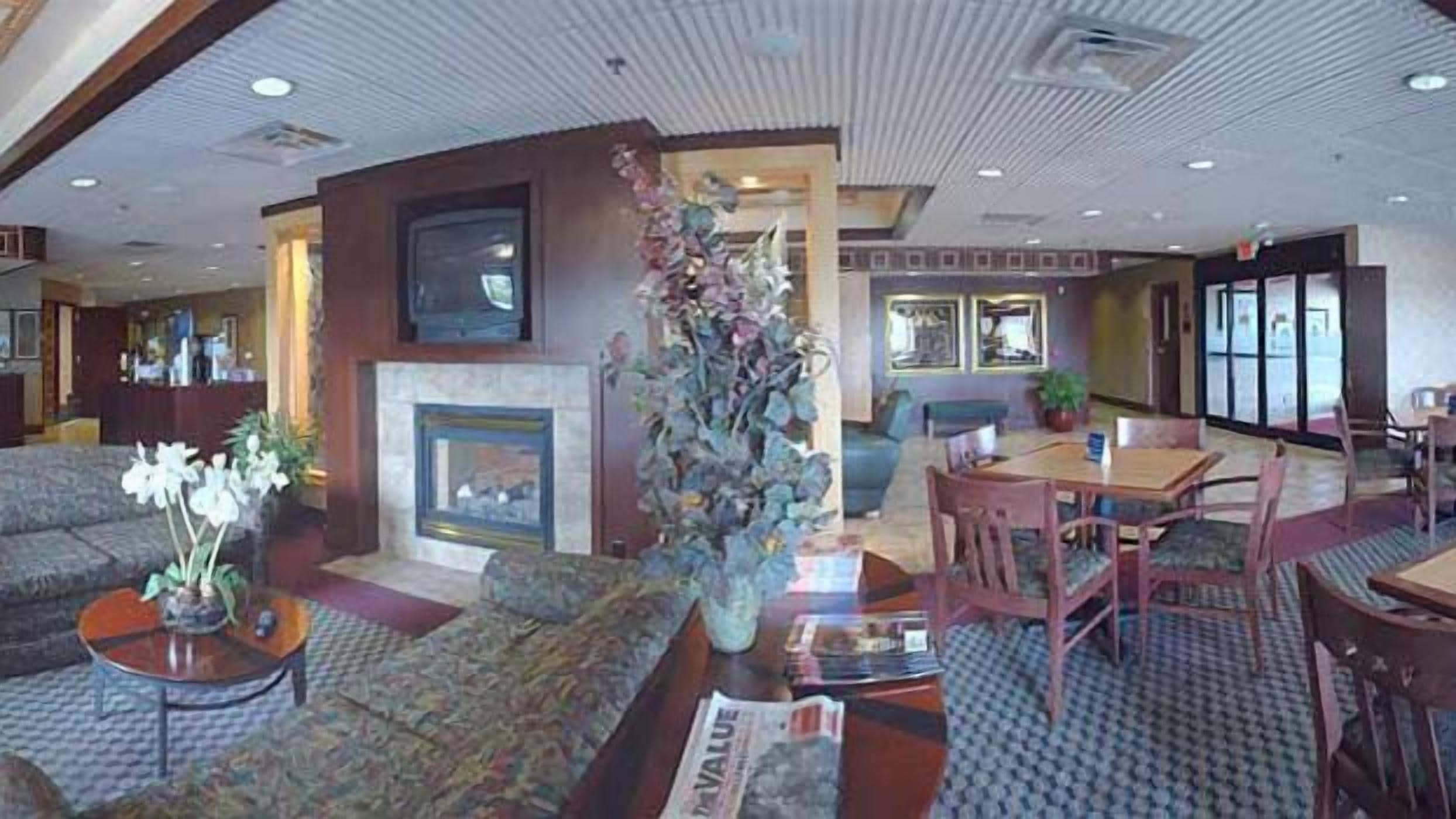 A hotel lobby with a fireplace, seating area, and a dining table.