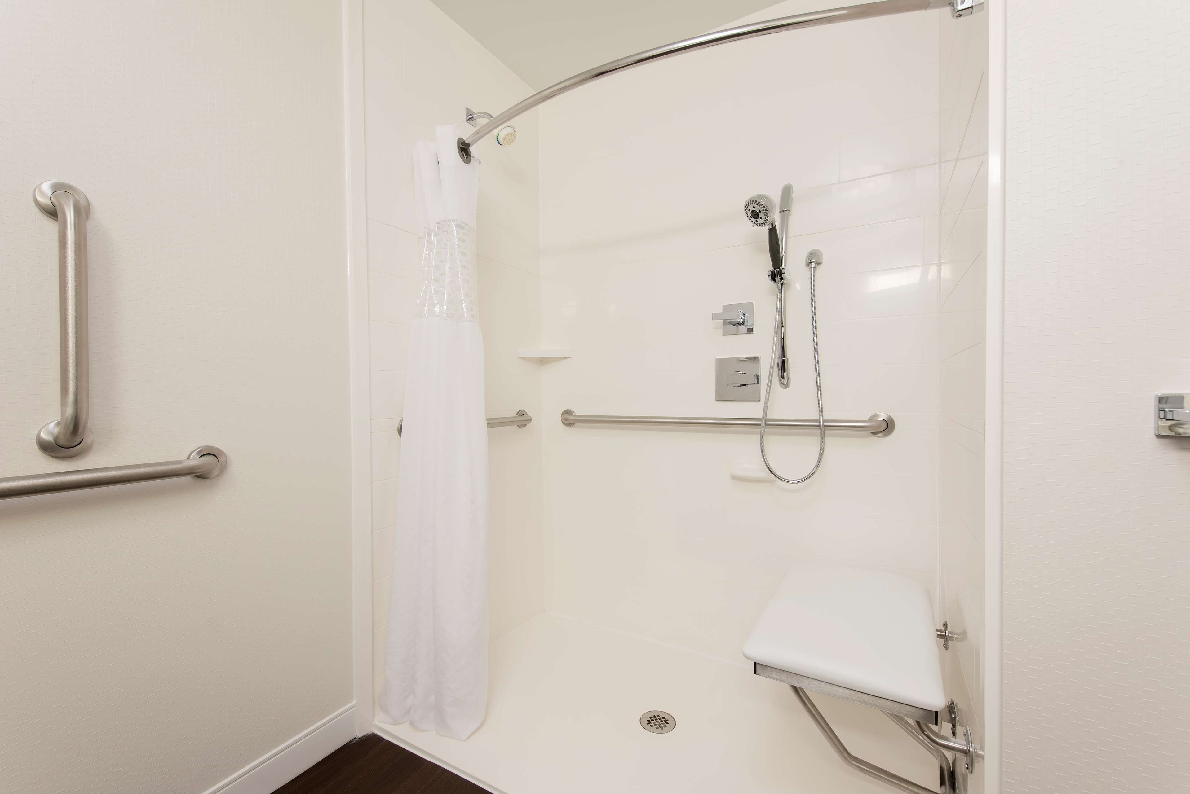 A bathroom with a shower, grab bars, a white toilet, and a showerhead.