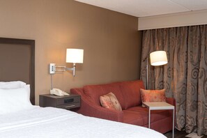 A hotel room with a bed, a red sofa, a small table, and a lamp.