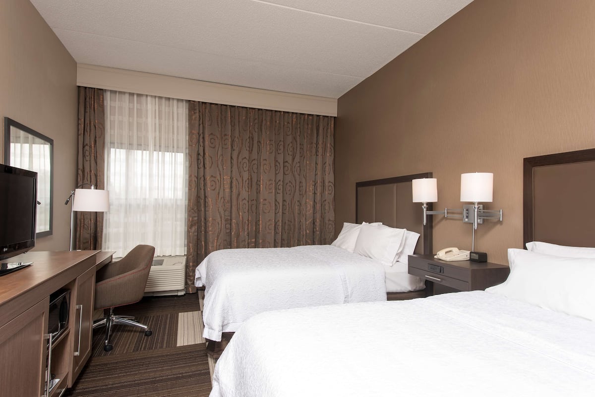 A hotel room with two beds, a desk with a television, a chair, a desk lamp, and a telephone.