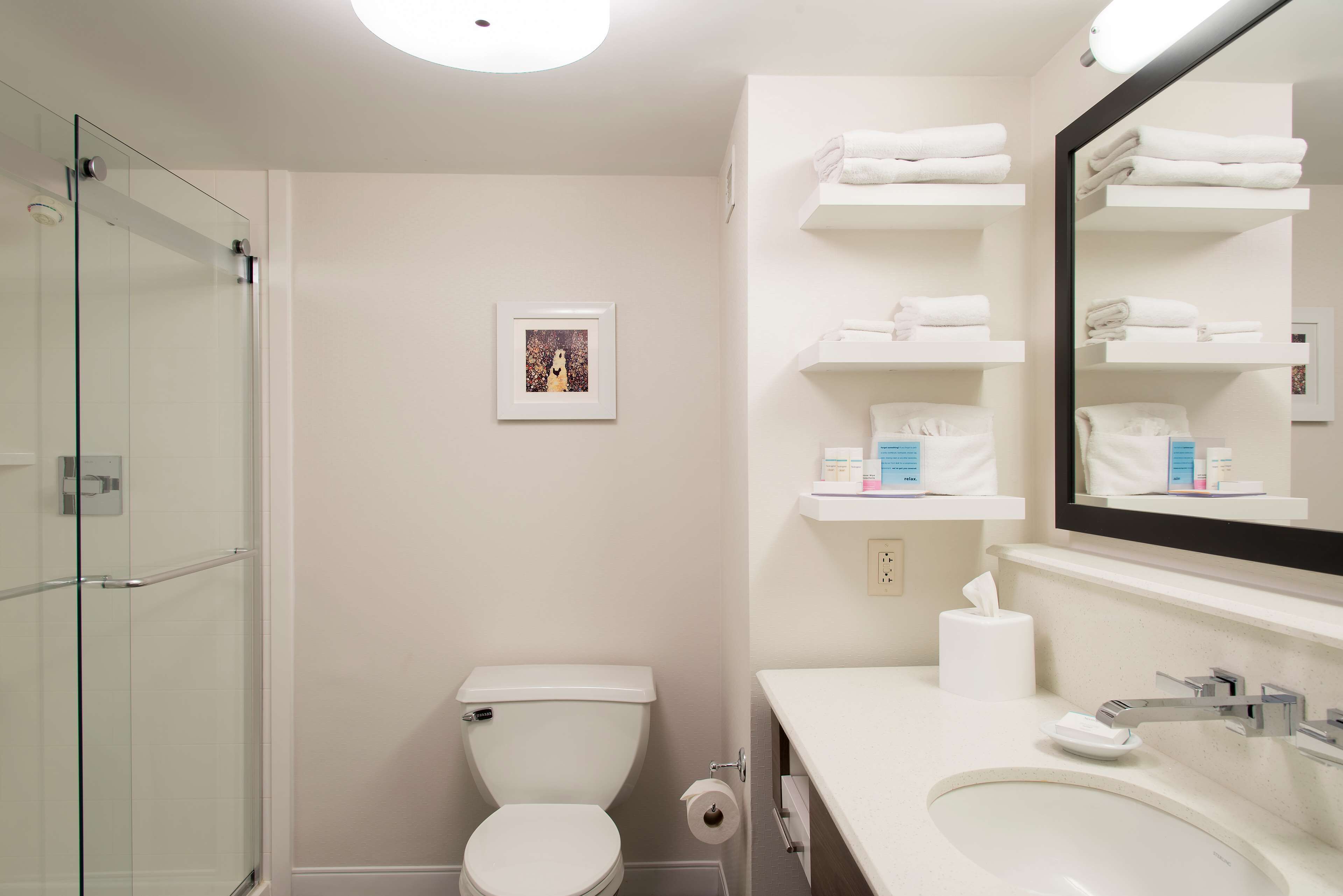 Un baño moderno con cabina de ducha de vidrio, inodoro, lavabo con espejo y repisas con toallas.